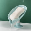 A leaf-shaped suction cup soap dish with a self-draining tray is shown, dripping water onto a white surface.
