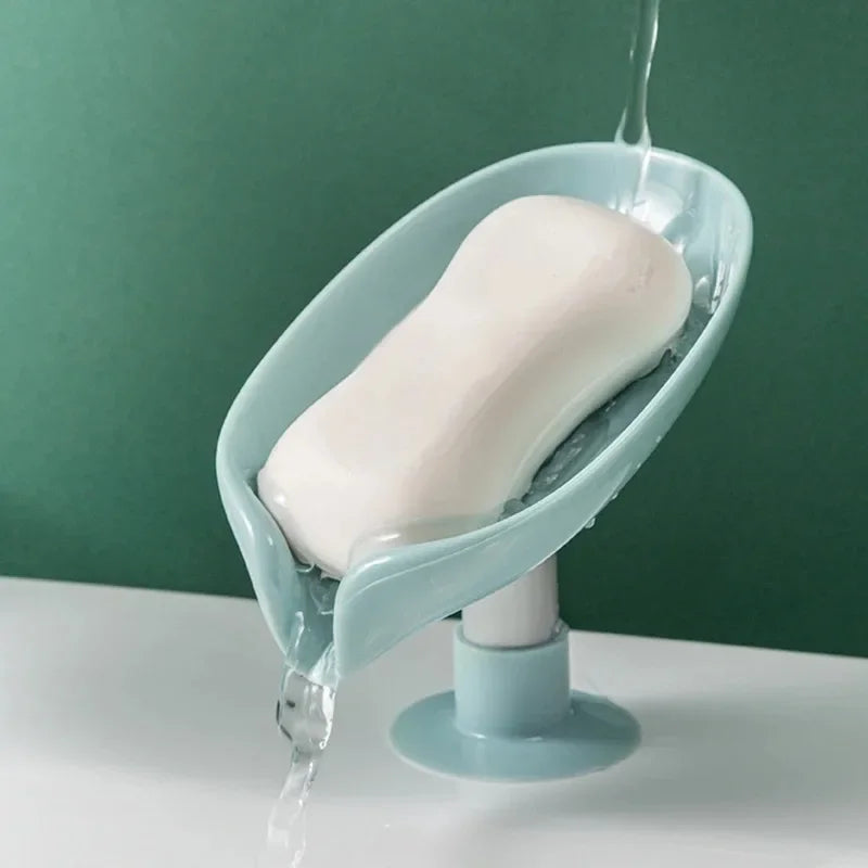 A leaf-shaped suction cup soap dish with a self-draining tray is shown, dripping water onto a white surface.