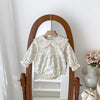 A white floral lace cotton romper for a baby girl hanging in a wooden-framed mirror.