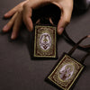 A hand holds a brown fabric scapular necklace with an ornate pendant against a dark background.