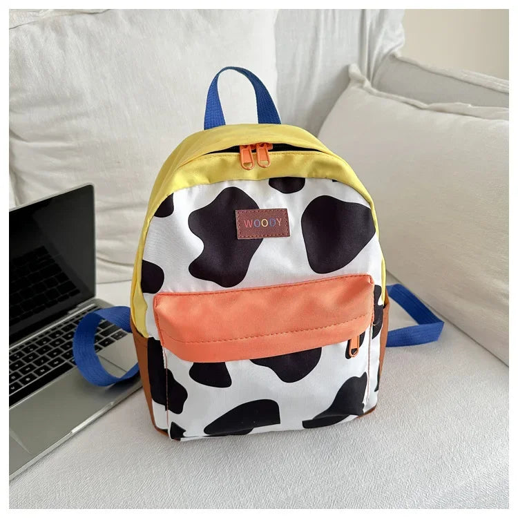 A yellow and black cow print backpack with orange accents resting on a white surface.