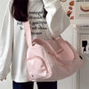 A pink large canvas travel tote bag with a strap is shown being held by a person wearing a white top.