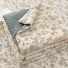 A stack of light beige fabric with a black floral pattern, likely a quilt or bedding, is shown on a surface.