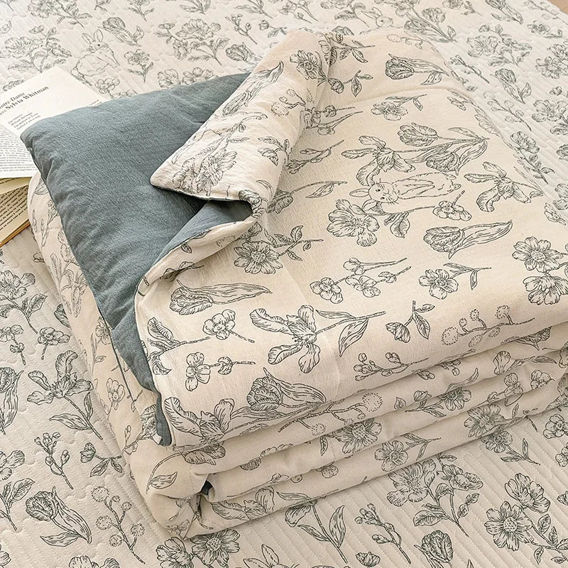 A stack of light beige fabric with a black floral pattern, likely a quilt or bedding, is shown on a surface.