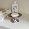 A white bottle of Press Milk and Make Puppy soap next to a silver ceramic soap dish.