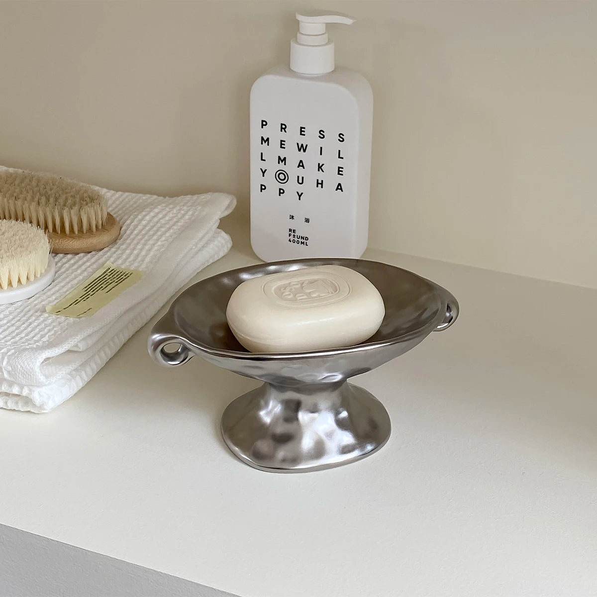 A white bottle of Press Milk and Make Puppy soap next to a silver ceramic soap dish.