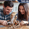 A man and a woman are assembling a detailed wooden space shuttle model kit on a table.