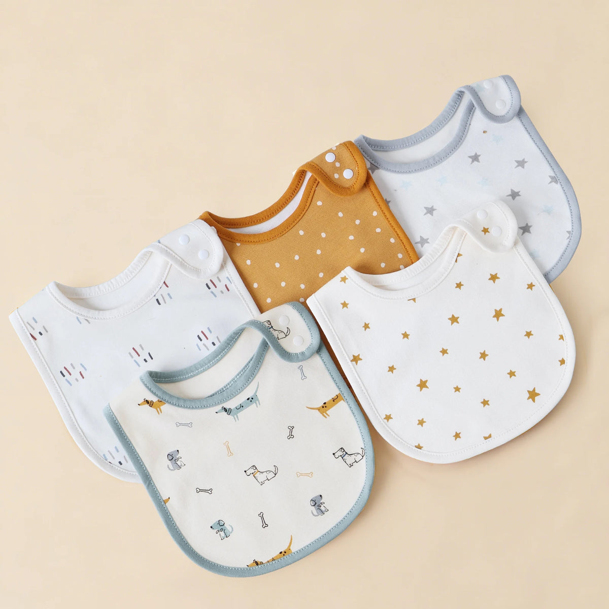 A collection of three cotton baby bibs in white, mustard yellow, and light blue with star patterns.