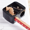 A black automatic dual-hole pencil sharpener is shown with a wooden pencil inserted for sharpening.