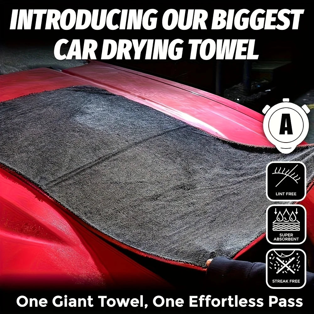 A close-up of a large gray microfiber drying towel being used to clean the surface of a red car.