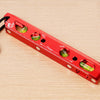 A red magnetic aluminum level ruler with V-grooves for precise angle measurement is shown on a wooden surface.