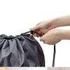 A gray drawstring laundry bag is shown being filled with white fabric inside a light-colored bag.