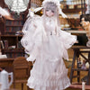 A white, frilly doll with long hair and a lace dress stands in an antique setting.