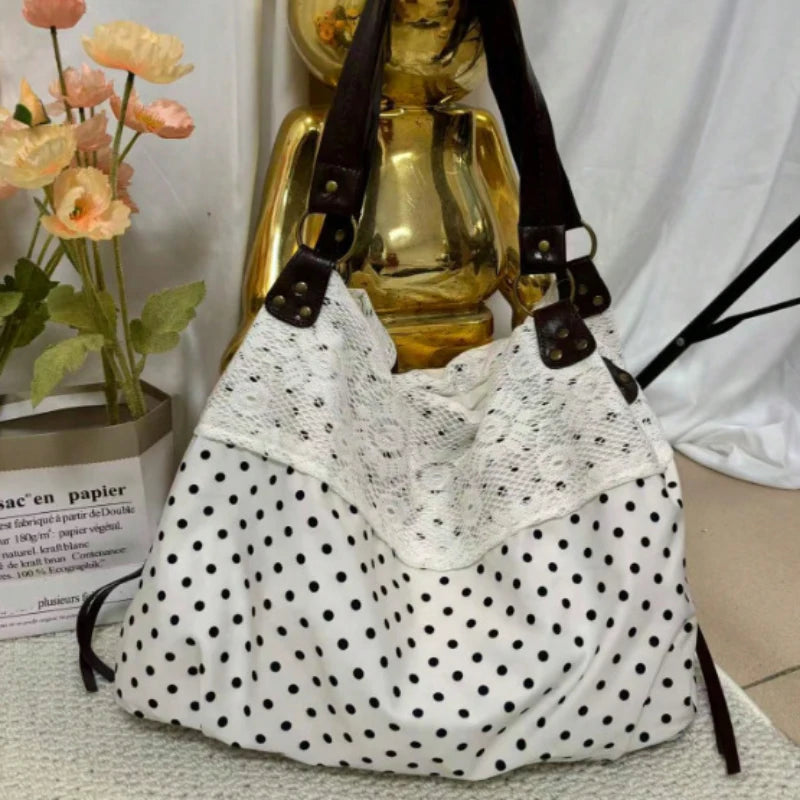 Sac à l'épaule à motifs blancs avec sangles en cuir noir et un objet décoratif doré en arrière-plan.