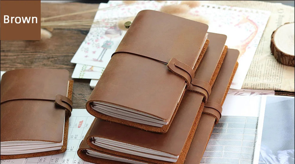 A stack of brown genuine leather refillable journals resting on a wooden surface with paper and tools.