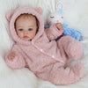 A newborn Reborn baby doll wearing a pink fuzzy hooded outfit lying on white fur.