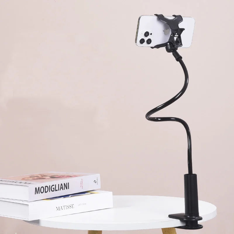 A black flexible gooseneck phone holder with a white smartphone attached, resting on a white table.