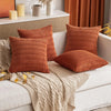A set of three rust orange corduroy throw pillow covers with a striped boho design resting on a white sofa.