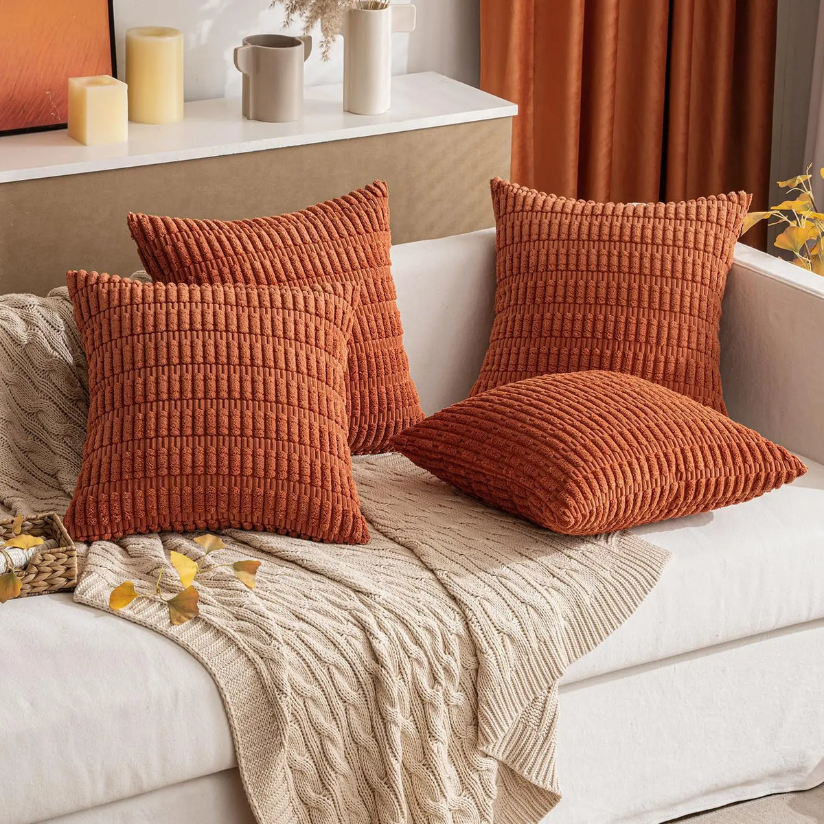 A set of three rust orange corduroy throw pillow covers with a striped boho design resting on a white sofa.