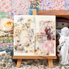 An open scrapbook shows floral paper sheets and decorative elements for journaling and crafts.