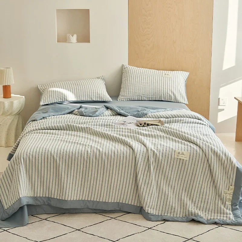 A light blue and white striped breathable summer quilt is displayed on a bed with a wooden headboard.