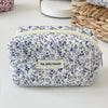 A quilted floral makeup bag with a white background and blue and purple flowers, featuring a zipper closure.