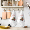 A set of white kitchen towels featuring Christmas themed red pickup trucks and greenery.