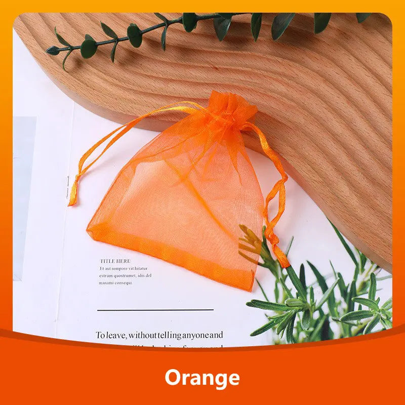 An orange organza drawstring gift bag tied with twine resting on a wooden cutting board.