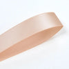 A roll of double face satin ribbon in a nude pink color shown diagonally.