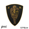 A black shield patch with gold lettering and an archangel design featuring St. Michael's cross.