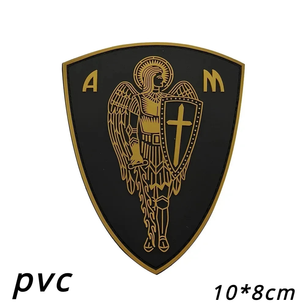 A black shield patch with gold lettering and an archangel design featuring St. Michael's cross.