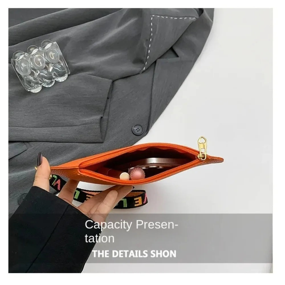 Orange heart-shaped PU coin purse with a black wrist strap shown against a gray blazer.