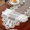 A dark wooden table is decorated with an embroidered mesh lace table runner featuring white lace and gold accents.
