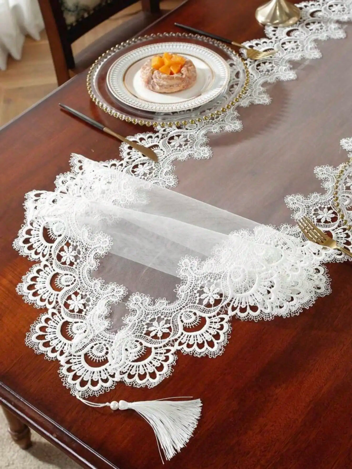 A dark wooden table is decorated with an embroidered mesh lace table runner featuring white lace and gold accents.