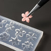 A silicone nail art mold featuring a pink floral design is being pressed by a fine tool.