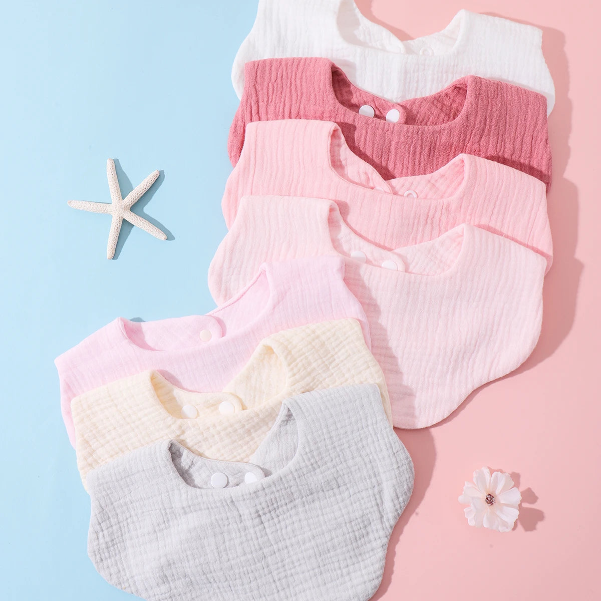 A stack of three soft cotton baby bibs in pink and white shades with ruffle trim arranged on a light blue background.