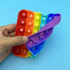 A hand holds a colorful 2-in-1 alphabet and number fidget popper toy with various colored buttons.