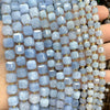 A hand holds a strand of light blue and lavender square faceted natural stone beads for jewelry making.