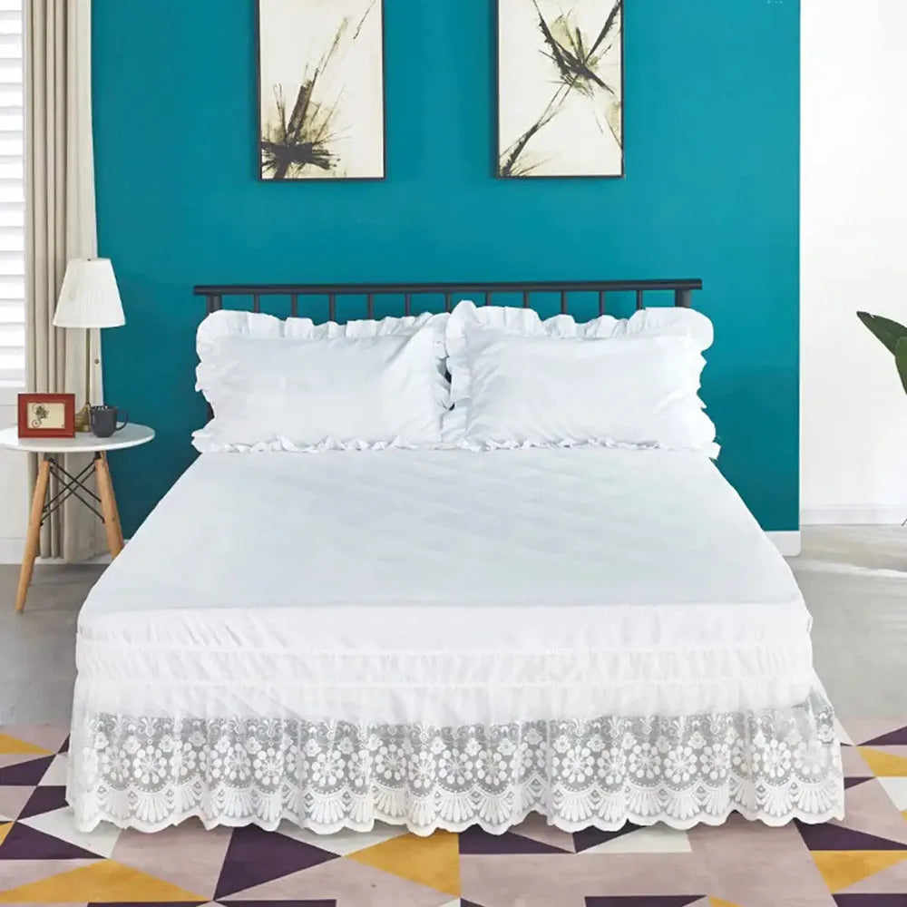 A white bed featuring a ruffled lace skirt and white bedding against a teal accent wall.