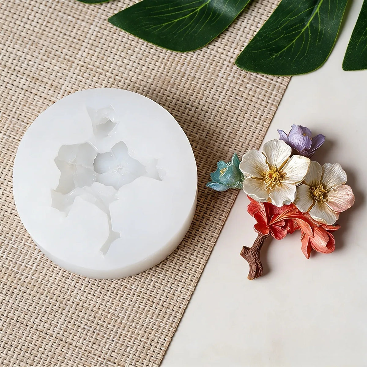 Un moule en silicone blanc en forme de fleur est exposé sur un tapis tissé avec des feuilles vertes.