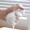A hand is squeezing a thick white foam or cleaning solution onto a surface.
