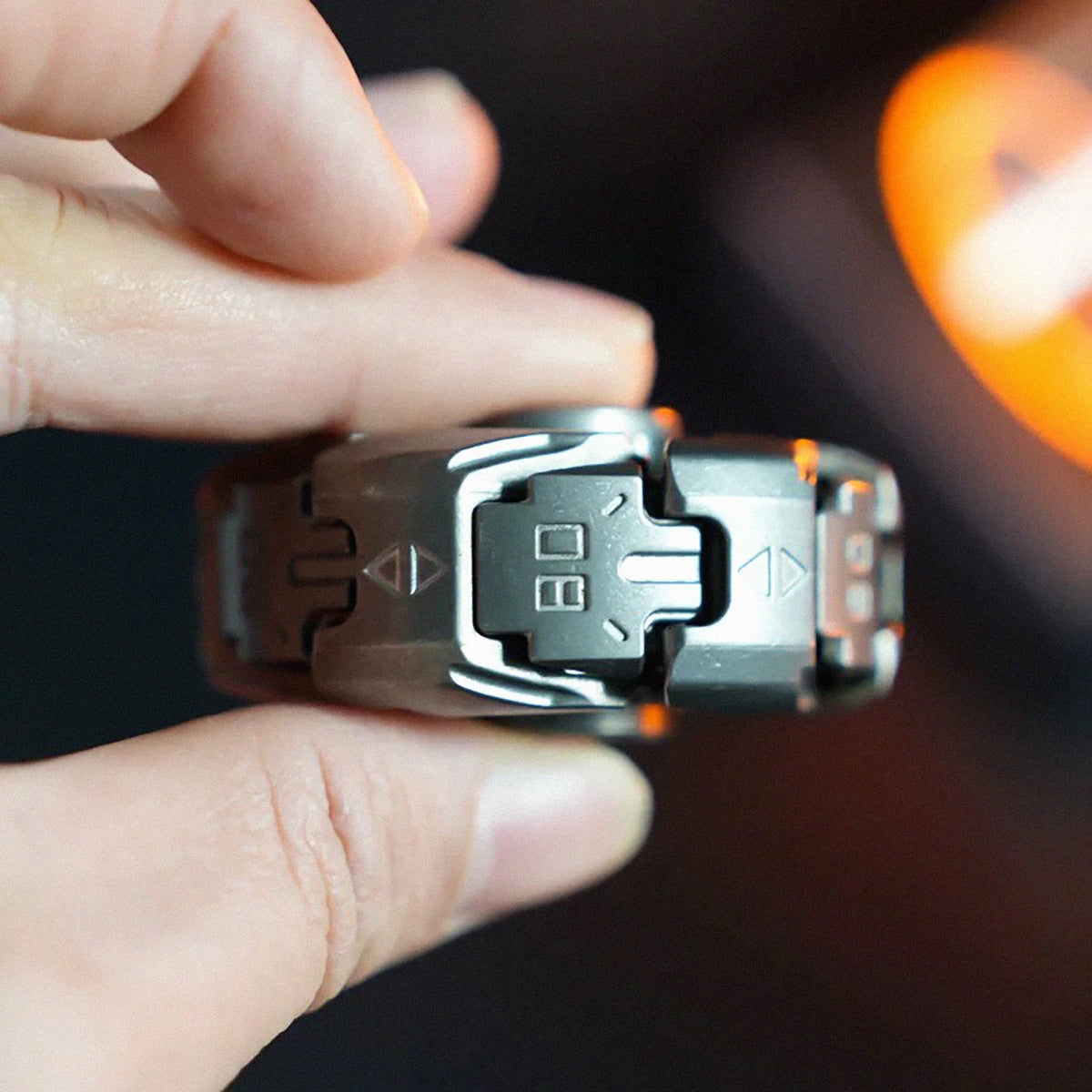 A hand holds a sleek stainless steel fidget spinner with multiple buttons and a spinning top.