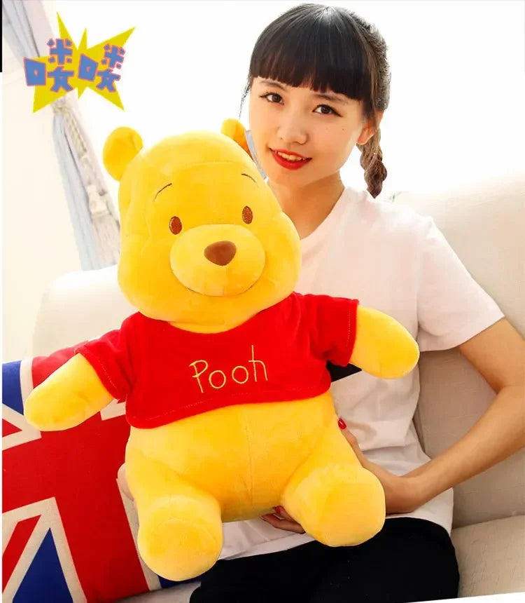 A young woman is holding a yellow Winnie the Pooh plush toy on a white couch.