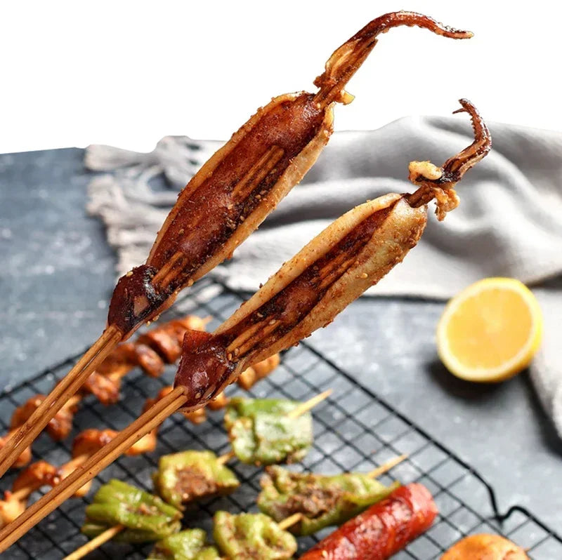 A set of natural bamboo skewers with grilled meat and vegetables are displayed on a black grill grate.