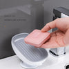 A hand places a pink leaf-shaped suction cup soap dish onto a white bathroom surface.