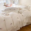 White duvet cover set with pink rose embroidery and lace details on a bed