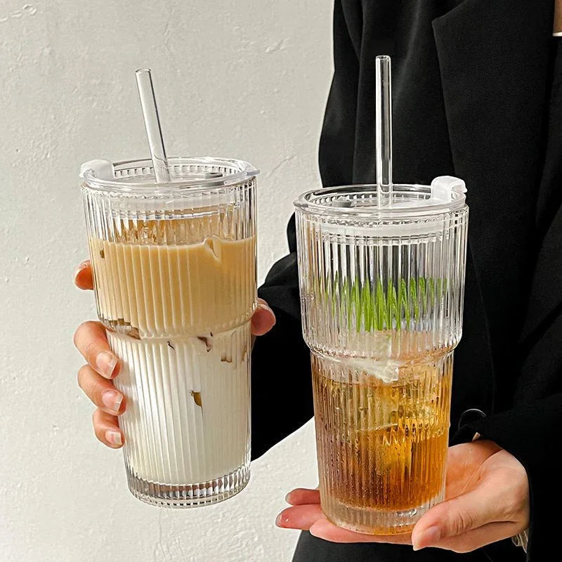 Une main tient un verre rempli de latte glacé, avec un motif rayé et une paille transparente.