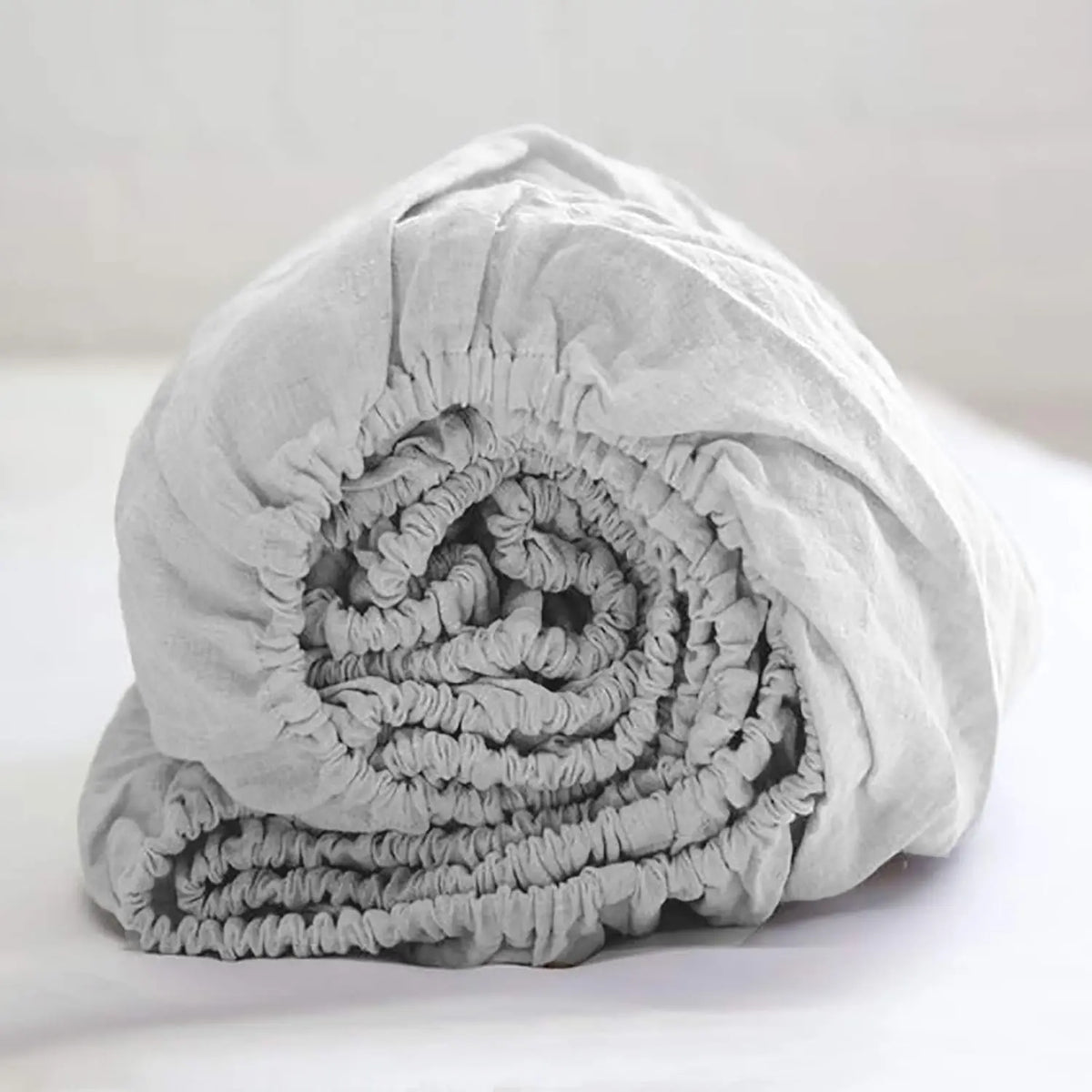 A tightly rolled light gray linen fitted sheet with deep pockets.