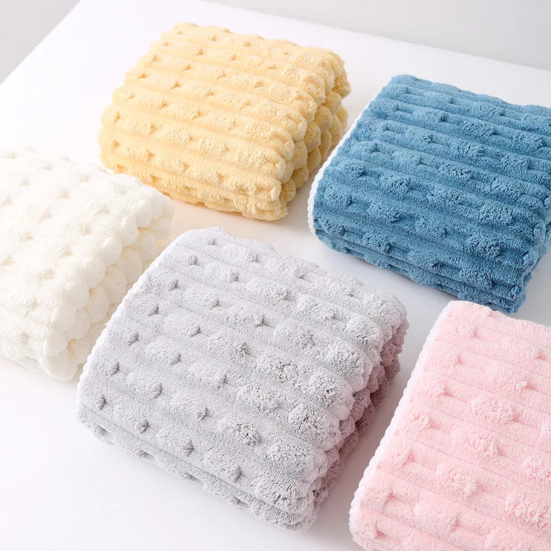 A collection of four textured bath towels in yellow, blue, gray, and pink arranged on a white surface.