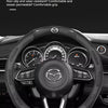 A black carbon fiber steering wheel cover is shown on a Mazda vehicle's steering wheel.